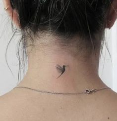 a woman's neck with a small bird tattoo on the back of her neck