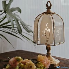 a glass lamp sitting on top of a wooden table next to flowers and a potted plant