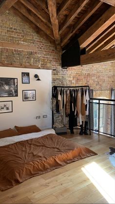 a bed in a bedroom next to a brick wall with clothes hanging on the rails