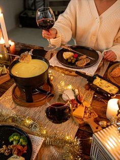 a woman sitting at a table holding a wine glass in front of food and candles