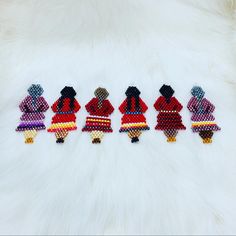 five beaded native american women in colorful outfits on a white fur surface, with one woman wearing a red dress