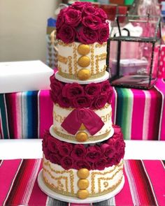 a three tiered cake with red roses on it's sides and gold accents