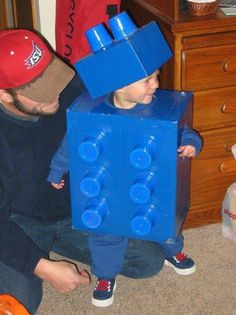 a man and his son are playing with legos in the living room, one is wearing a blue box