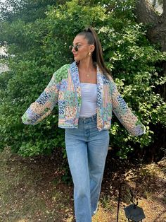 a woman walking in the grass with her hand on her hip, wearing jeans and a colorful jacket