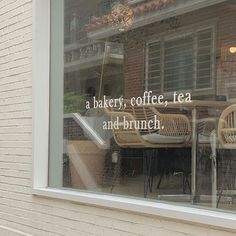 the reflection of a table and chairs in a window with a brick building behind it that reads, a bakery, coffee, tea and brunch