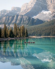 two people in a boat on a lake surrounded by mountains