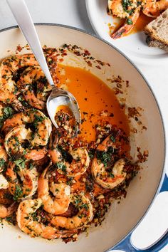 a bowl filled with shrimp and sauce on top of a white table next to bread