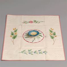 an embroidered tablecloth with flowers and leaves on the border is displayed in front of a gray background