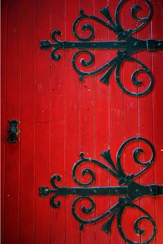 an iron gate on the side of a red door that has been painted with black paint