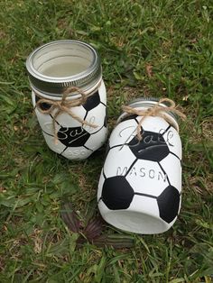 two mason jars decorated with soccer balls are sitting on the grass in front of a field