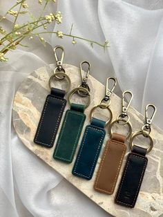 four leather key fobs on a marble slab with flowers in the back ground