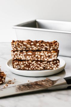 three pieces of chocolate peanut butter granola bars on a plate next to a knife