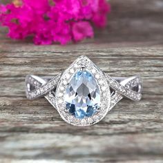 a blue and white diamond ring sitting on top of a wooden table next to pink flowers