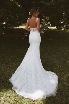 a woman in a white wedding dress standing on grass with her back to the camera