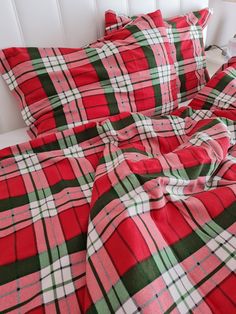 a red and green plaid comforter set on a bed with white headboard in the background