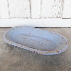 an old white bowl sitting on the ground in front of a door with peeling paint