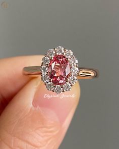 a close up of a person's hand holding a ring with a pink diamond