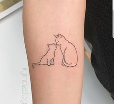 a couple of cats sitting next to each other on a person's arm with a small tattoo