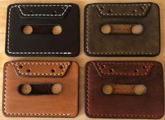 four leather wallets with holes in them sitting on a wooden table next to each other