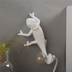 a white geckoe figurine on the wall next to a light bulb