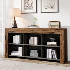 a book shelf with books on it in front of two framed pictures and a lamp