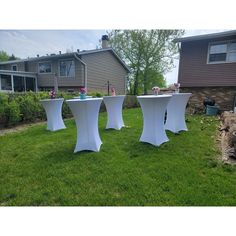 three white tables sitting on top of a lush green field in front of a house