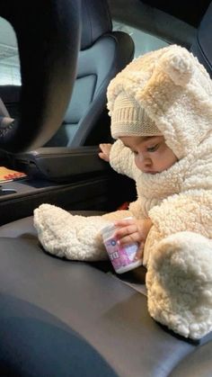 a baby sitting in the back seat of a car with a stuffed animal on it's arm