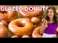 a woman holding up a donut in front of a bunch of glazed donuts