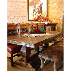 a wooden table with chairs around it and a painting on the wall behind it in a room that has brick walls