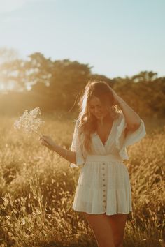 a woman standing in a field with her hands on her head and holding a flower