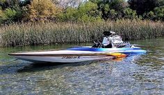 a motor boat with two people in it on the water near some grass and trees