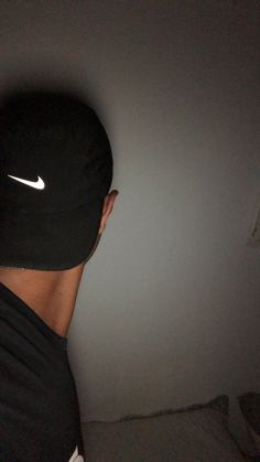 a man wearing a black hat with the nike logo on it's side in front of a white wall