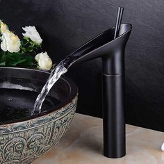 a black faucet is pouring water into a bowl with flowers in the background