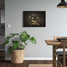 a potted plant sitting on top of a wooden table next to a wall mounted painting