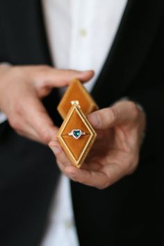 a man in a tuxedo is holding a ring with an emerald on it