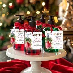 three bottles of soap sitting on top of a white cake plate next to a christmas tree