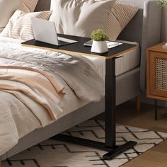 a laptop computer sitting on top of a table next to a bed with pillows and blankets