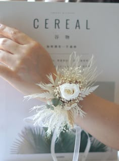 a woman's hand holding a white flower and feather corsage on her wrist