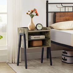 a nightstand with a clock and books on it next to a bed in a bedroom