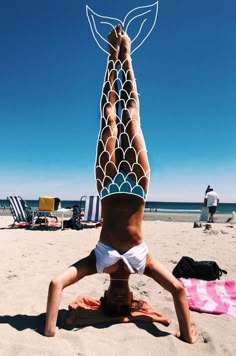 a woman doing a handstand on the beach with her legs spread wide apart