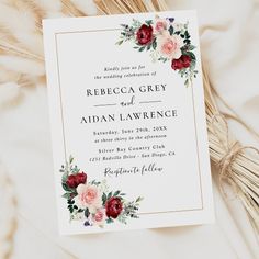 a wedding card with flowers and greenery on the front is laying next to some dried grass