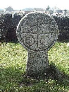 a headstone in the middle of a field with grass and stone walls behind it