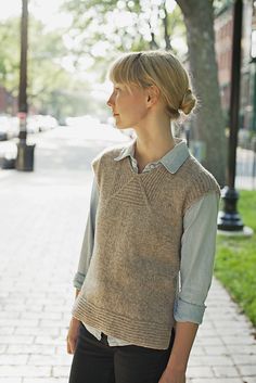 a woman is standing on the sidewalk wearing a sweater and black pants with her hands in her pockets