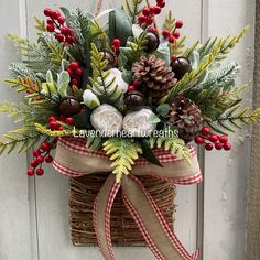 a christmas wreath with pine cones, berries and greenery hanging on the front door