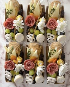 an assortment of cheeses, fruits and flowers arranged in small trays on a marble surface