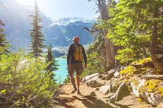 a man hiking up a trail in the mountains with trees and water on either side