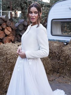 a woman in a white dress standing next to a pile of hay and a camper