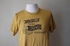 Let your Sandwich Flag fly with this Mustard Yellow Danielle Ate the Sandwich T-shirt designed by Ryan Polich. Printed on heather mustard yellow Bella + Canvas Shirts black ink. Shirts are available in adult SMALL, MEDIUM, LARGE, and X-LARGE unisex sizes, super soft to the touch, nice stretch, washable, runs long/lean, but drapes well on the body. Fiber Content: 52% Cotton 48% Polyester 100% Sandwich Printed by Oddities Print Shop in Kansas City, MO. Size shown is MEDIUM, Mustard Short Sleeve T-shirt With Graphic Print, Mustard Graphic Print Cotton T-shirt, Mustard Cotton T-shirt With Graphic Print, Casual Mustard Graphic Print T-shirt, Kansas City Mo, Flag Tshirt, Mustard Yellow, Print Shop, Kansas City