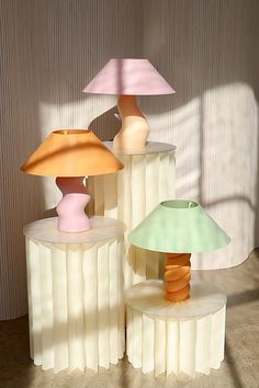 three different colored lamps sitting next to each other on top of a wooden table in front of a wall