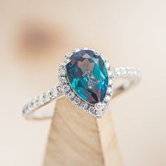 a ring with a blue topaz surrounded by white diamonds on a wooden stand in front of a blurry background